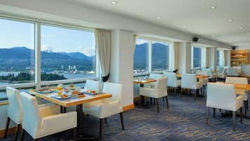 Een restaurant in een hotel met grote ramen met uitzicht op bergen, witte stoelen en een vloerbedekking in blauw.