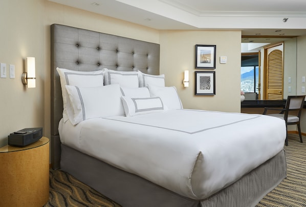 A large bed with a tufted headboard, white bedding, and a side table with a remote control. - Pan Pacific Vancouver (Vancouver)