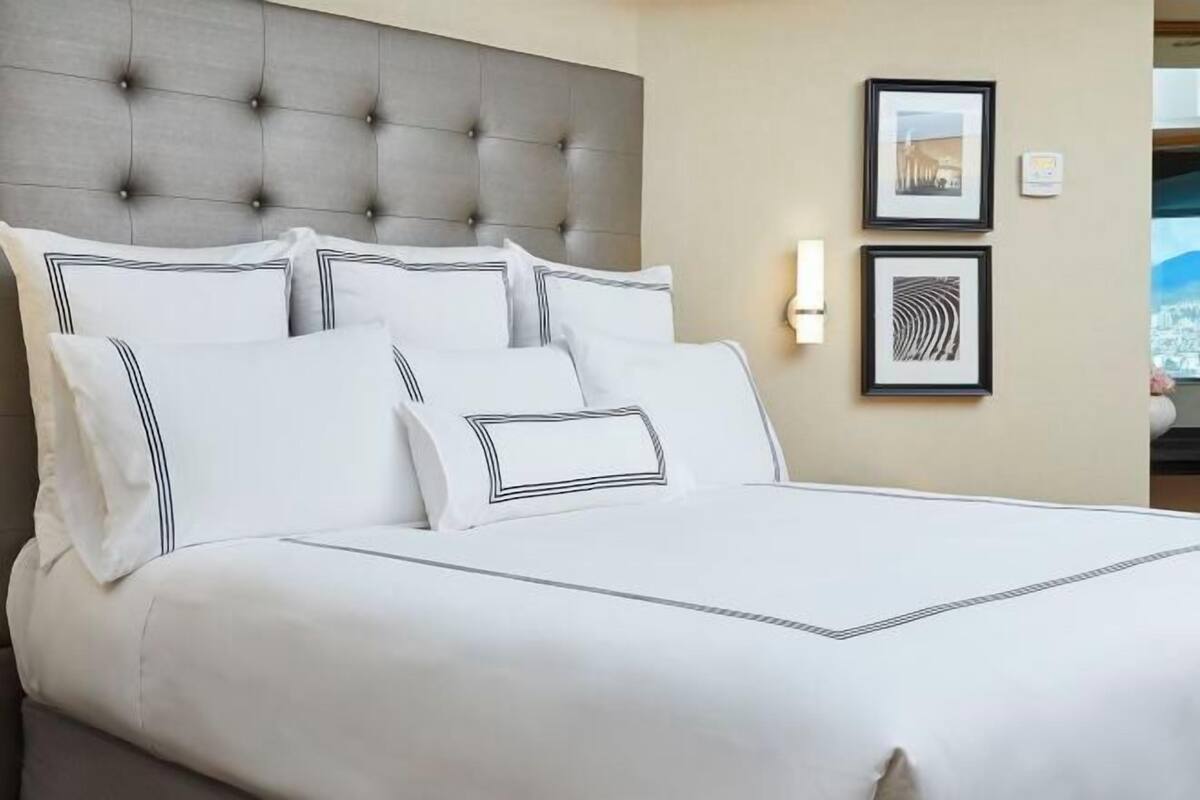 A hotel room with a tufted headboard, white bedding, and two framed pictures on the wall.