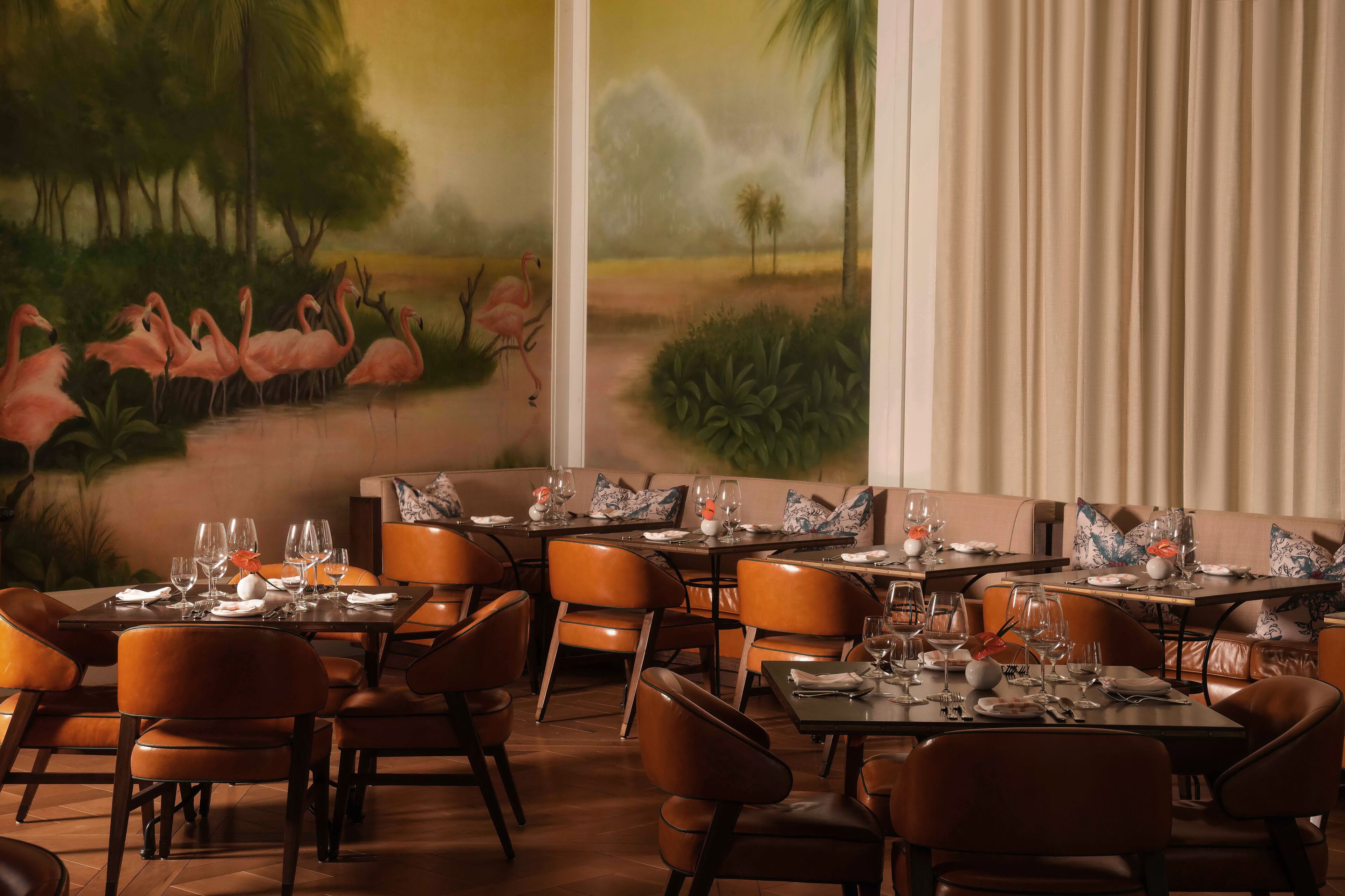 A restaurant with tables set for dining, chairs, and a mural of flamingos on the wall.