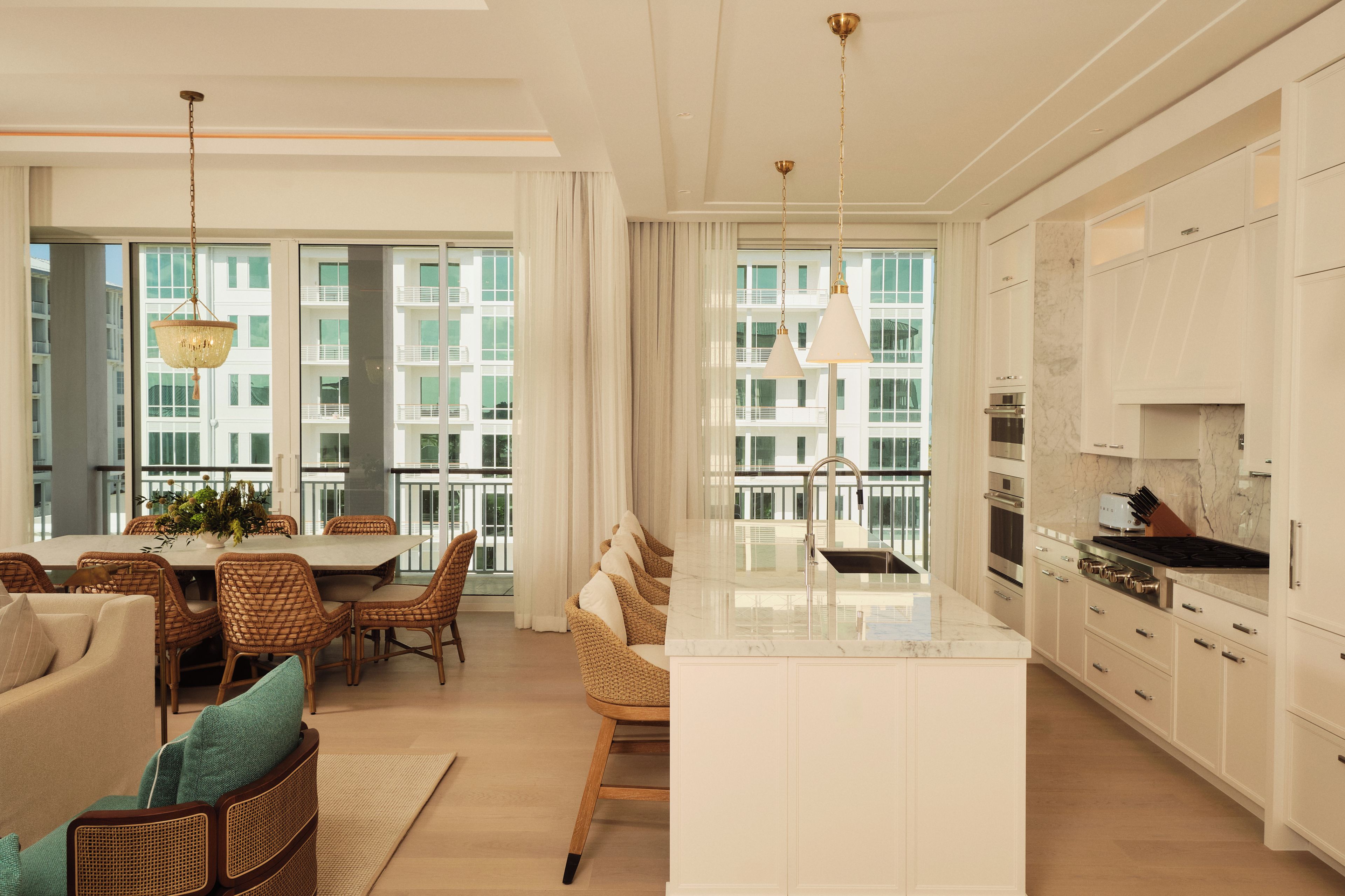 A modern kitchen with a central island, stainless steel appliances, and a view of a building through large windows.