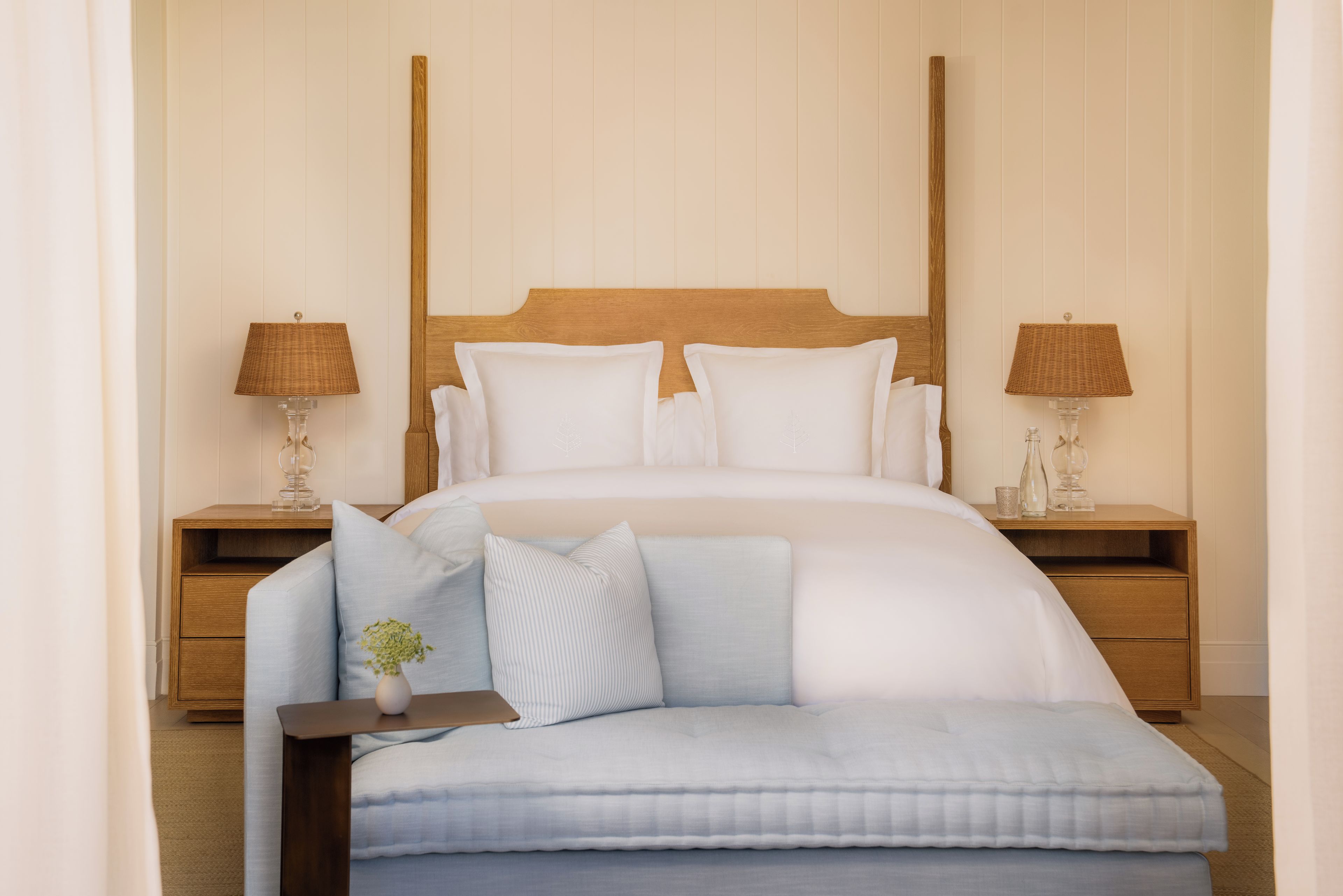 A neatly arranged bedroom with a large bed, two bedside tables with lamps, a nightstand, and a bench with a vase.