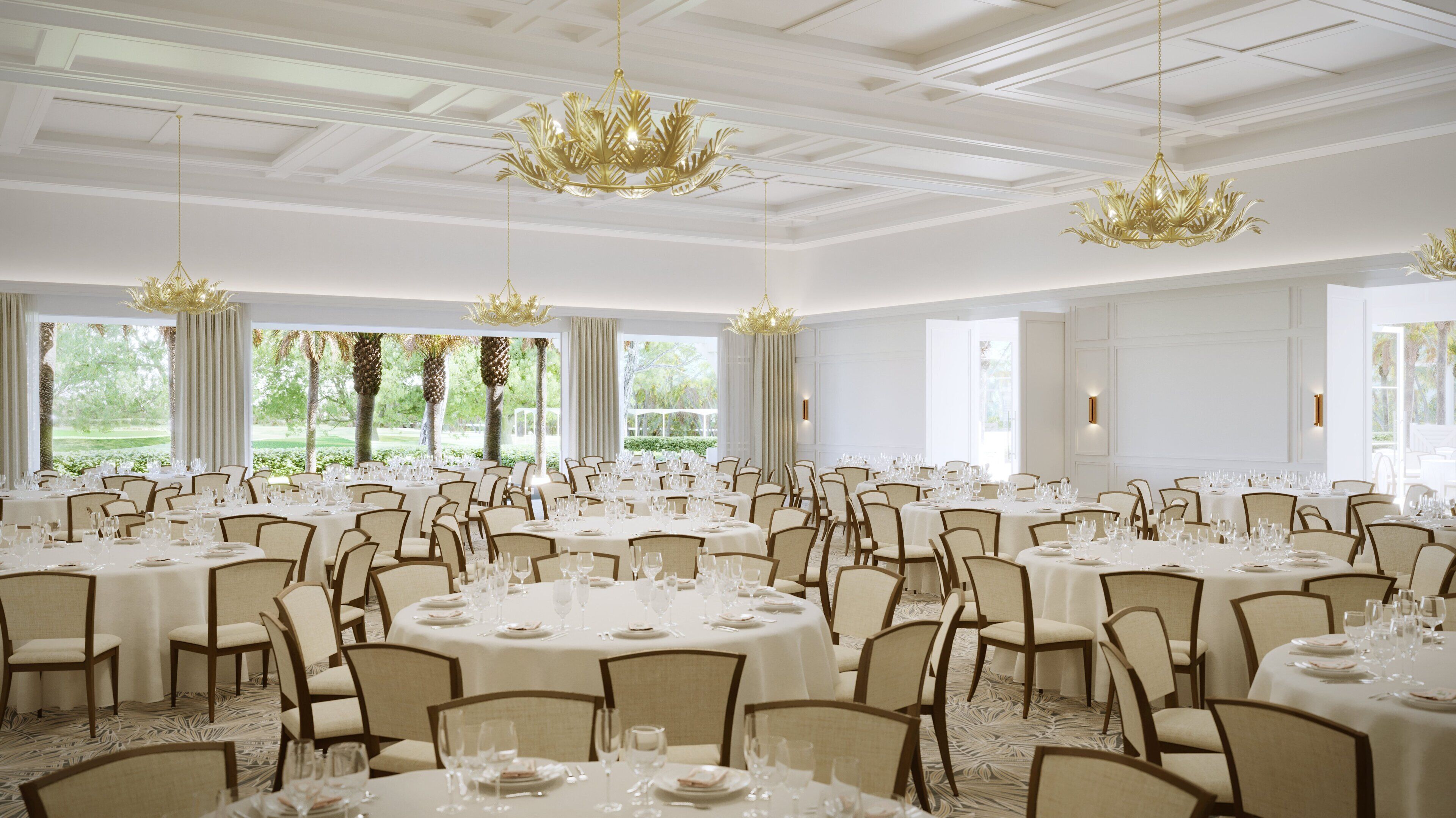 A large banquet hall with round tables set for dining, featuring chandeliers and large windows with curtains.