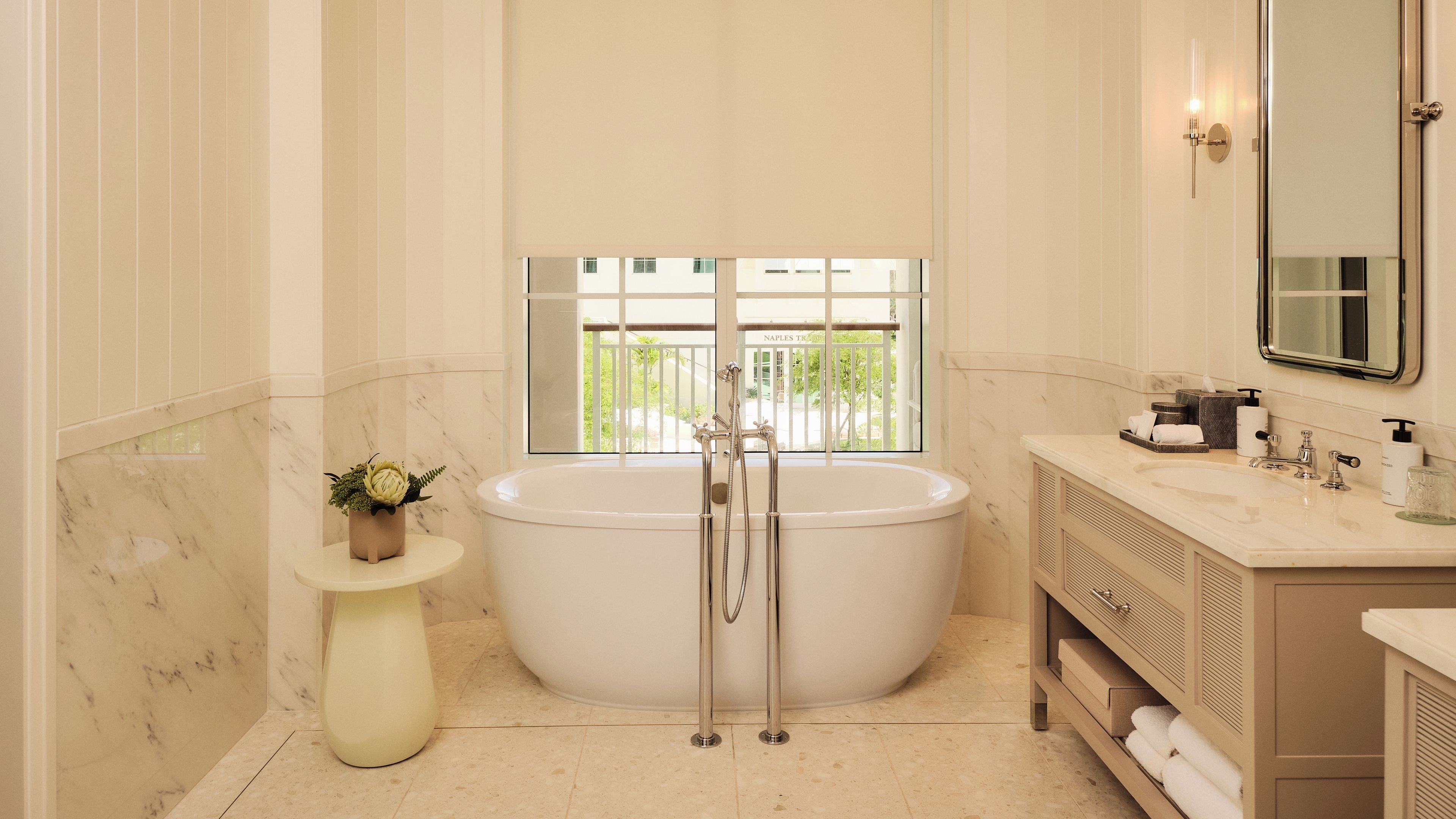 A bathroom with a large bathtub, a small round table with a plant, and a vanity with a mirror and toiletries.