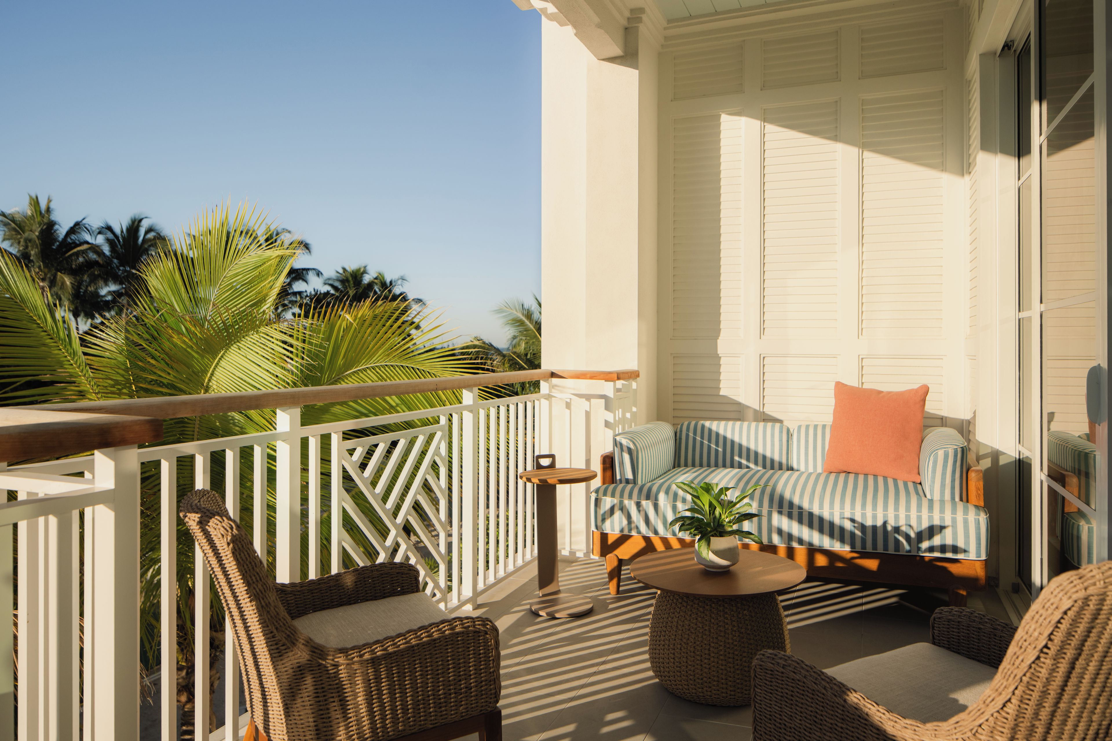 Ein Balkon mit Korbmöbeln, einem gestreiften Sofa und einem Blumentopf.