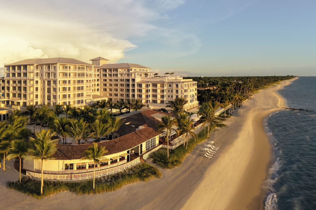 Ein Hotel direkt am Strand mit mehreren Gebäuden, einem Sandstrand und Palmen.