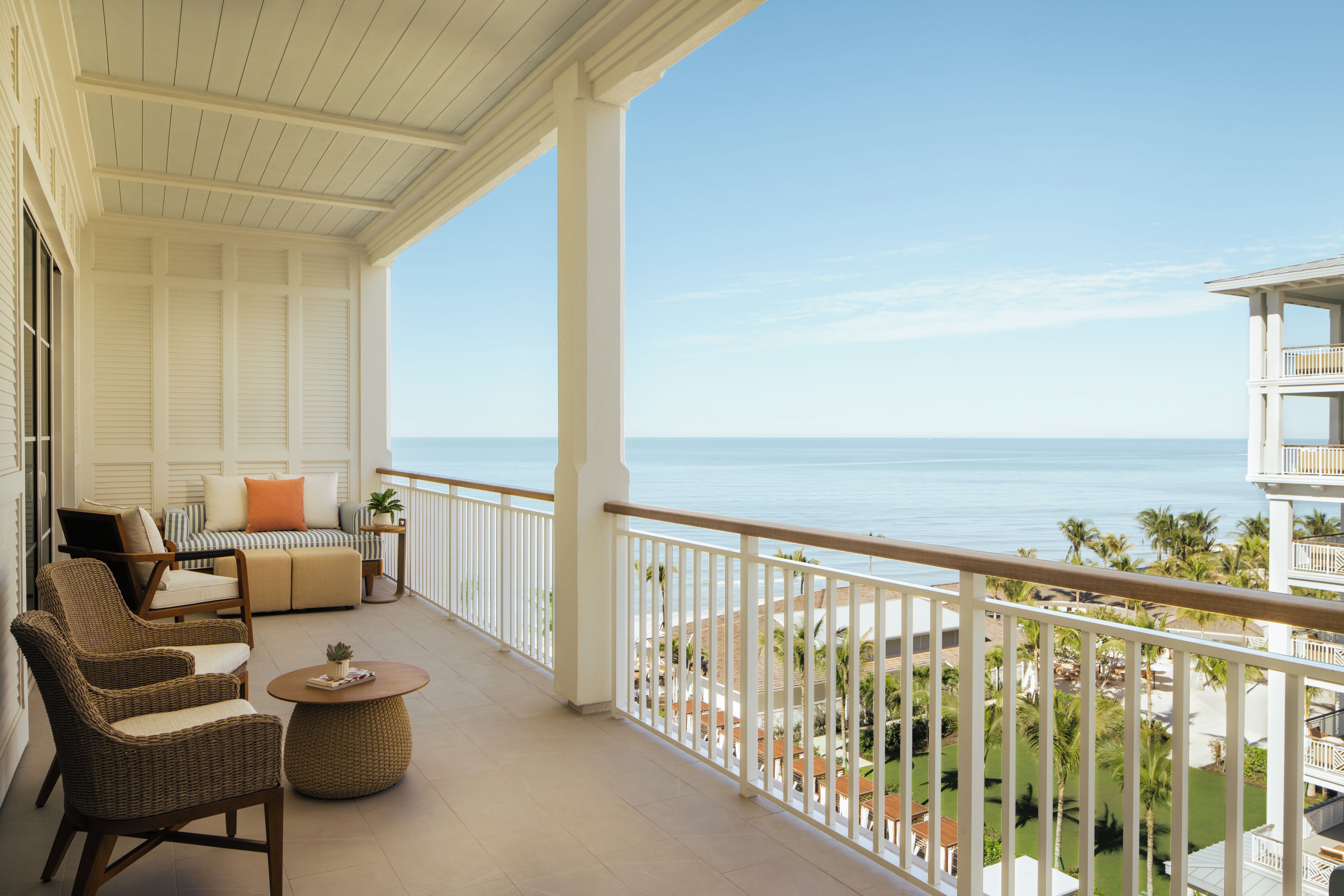 A balcony with wicker furniture, a view of the ocean, and a white railing.