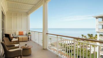 A balcony with wicker furniture, a view of the ocean, and a white railing.