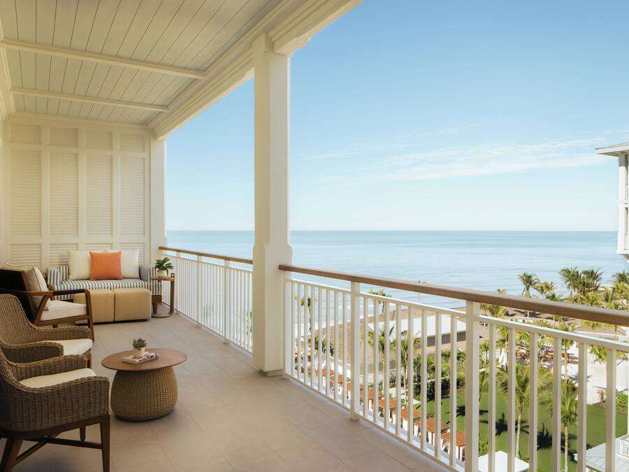 A balcony with wicker furniture, a view of the ocean, and a white railing.