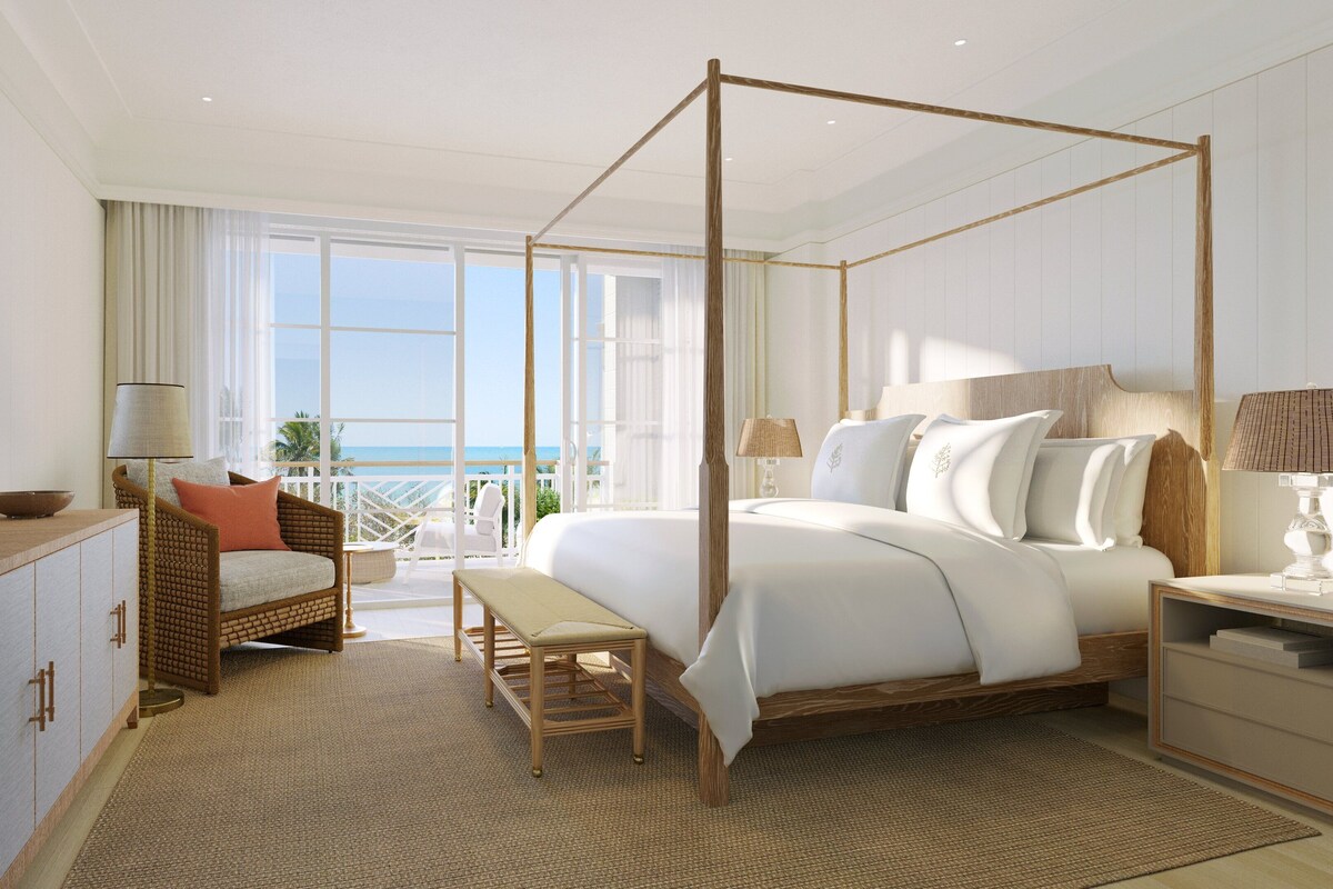 A spacious bedroom with a four-poster bed, a wooden bench, a wicker chair, a bedside table, and a flat-screen TV.