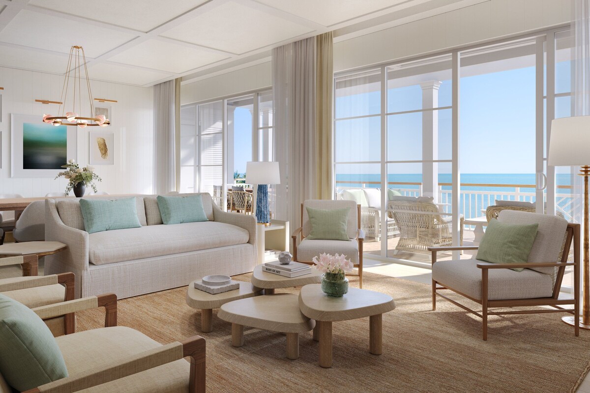 A spacious living room with a large window overlooking the ocean, a cozy seating area, and a dining table.