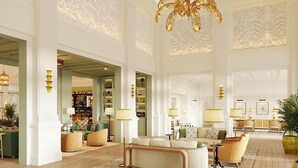 A spacious lobby with a high ceiling, ornate ceiling design, and a central chandelier. There are multiple seating areas with sofas and armchairs, and a large potted plant in the corner. - Naples Beach Club, A Four Seasons Resort (Naples)