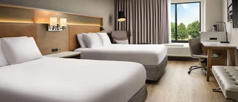 A hotel room with two beds, a desk, a chair, and a view of the outdoors.