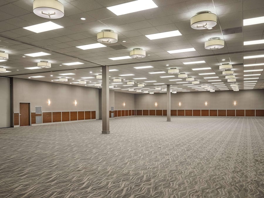 Una amplia sala de conferencias con alfombra estampada, luces de techo y paneles de madera a lo largo de las paredes.