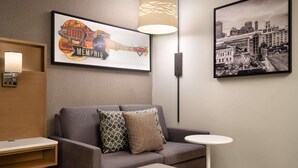 A hotel room with a sofa, a small table, a lamp, and two framed pictures on the wall. - Radisson Hotel West Memphis (West Memphis)