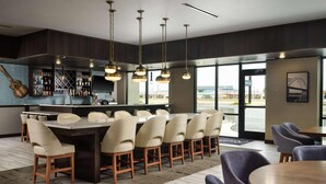 A modern bar area with a long counter, multiple hanging pendant lights, and a view of the outside through large windows. - Radisson Hotel West Memphis (West Memphis)