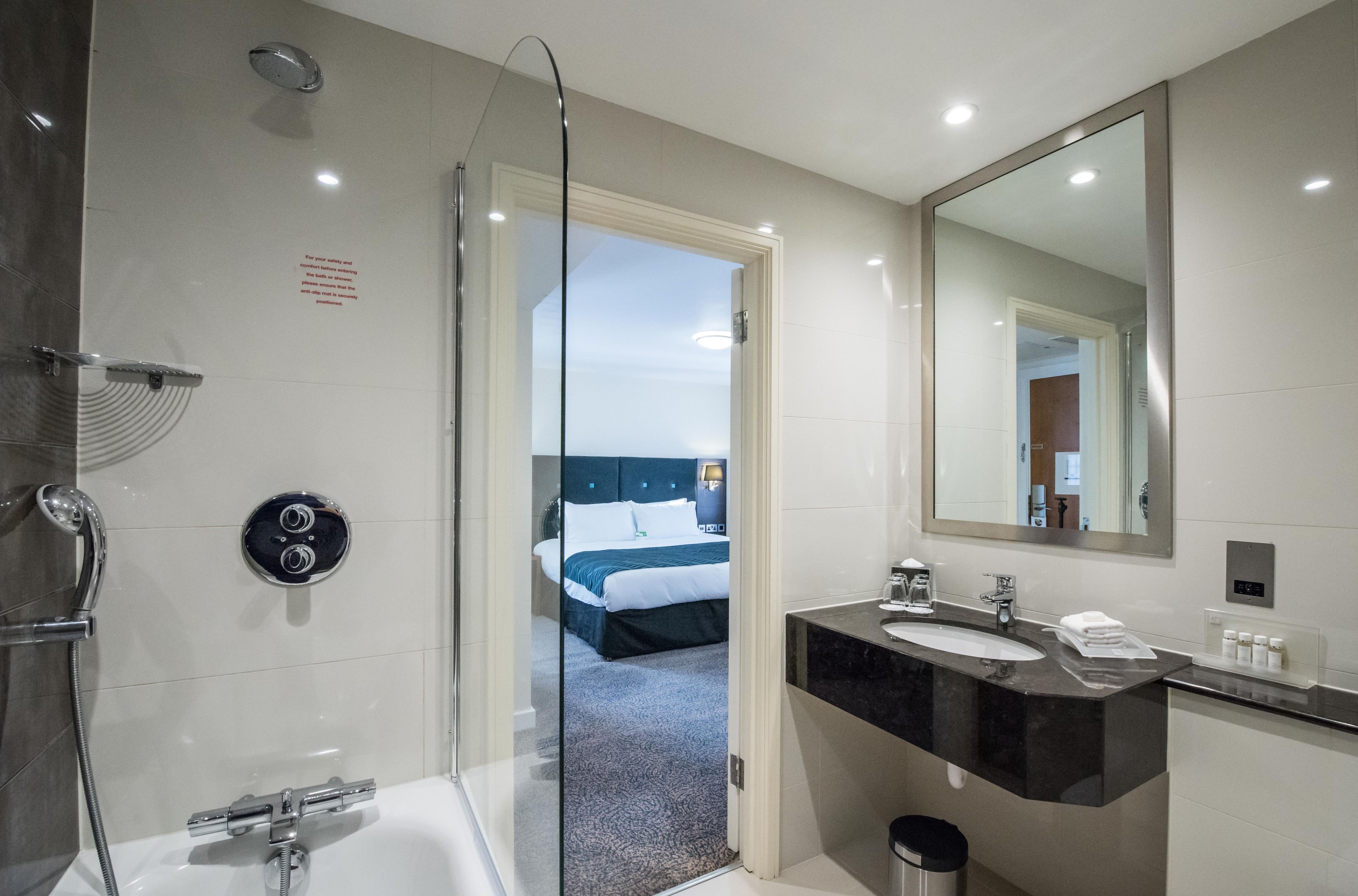 A modern bathroom with a glass shower enclosure, a bathtub, a large mirror, and a sink with a vanity.