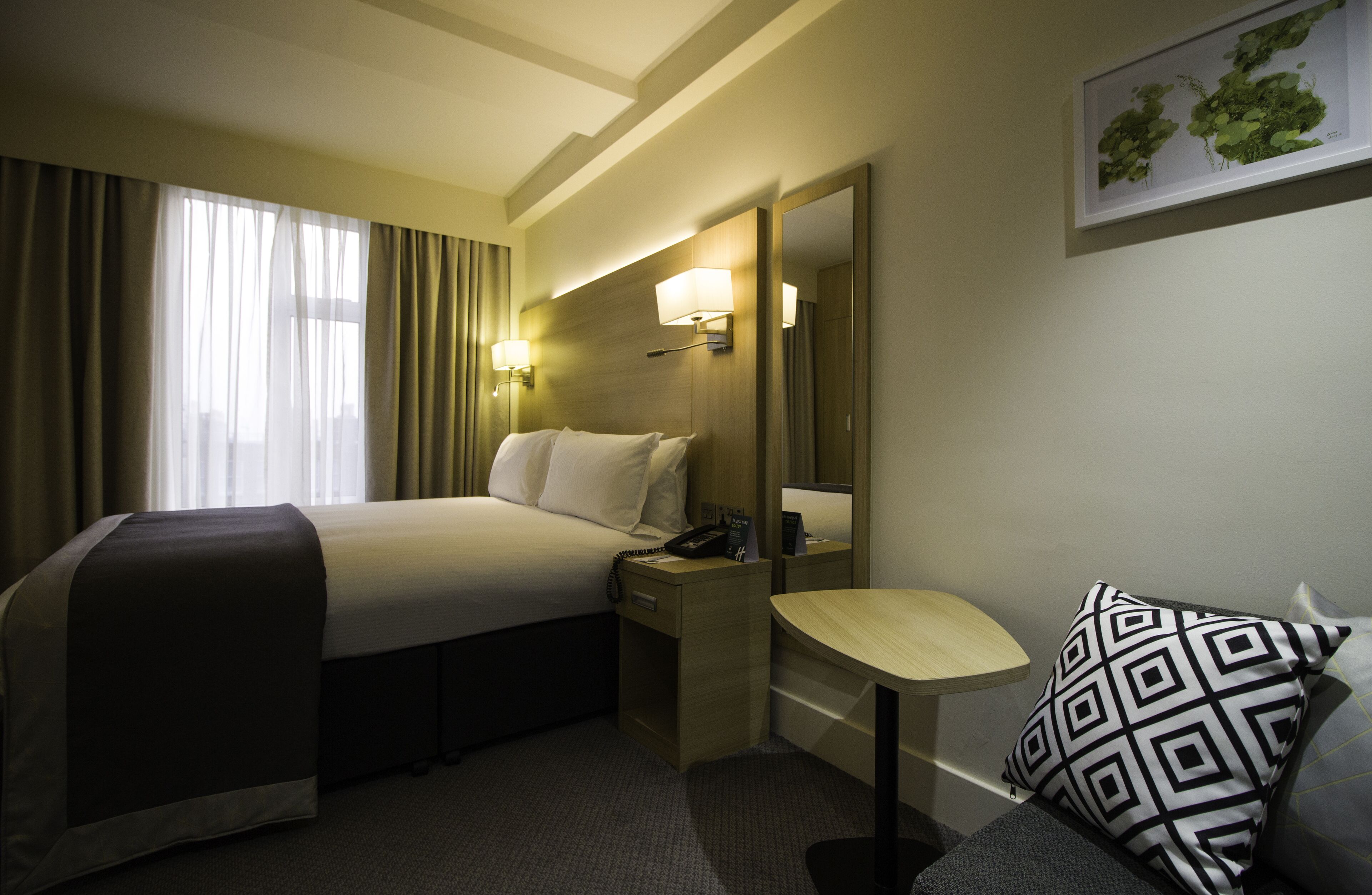 Ein Hotelzimmer mit Bett, Nachttisch, Lampe und kleinem Schreibtisch mit Stuhl.