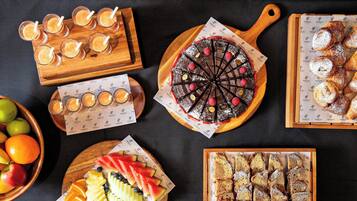 A variety of food items including a chocolate tart, pastries, fruit slices, and drinks on wooden boards.