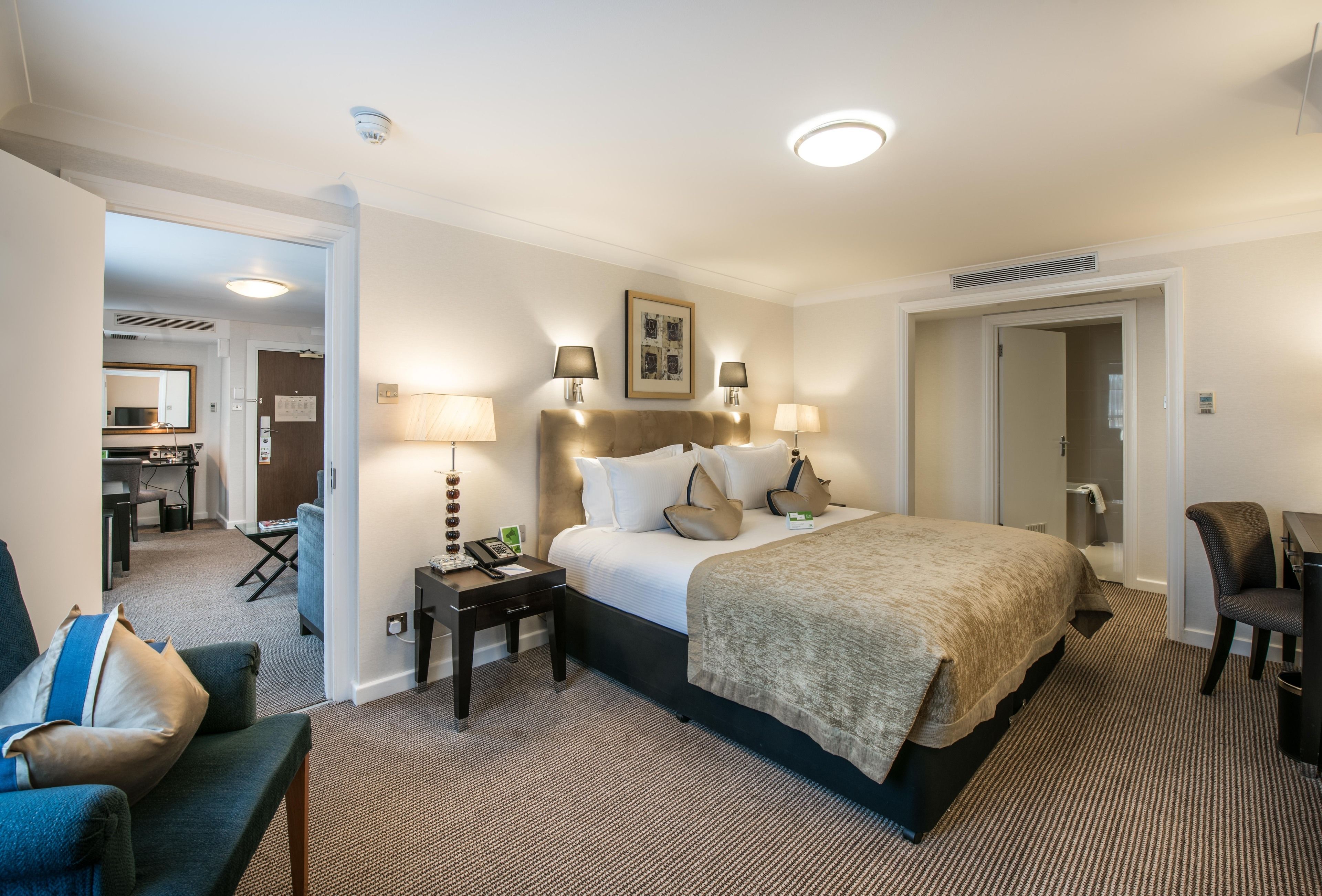 A hotel room with a large bed, two bedside tables with lamps, a desk, a chair, and a mirror.
