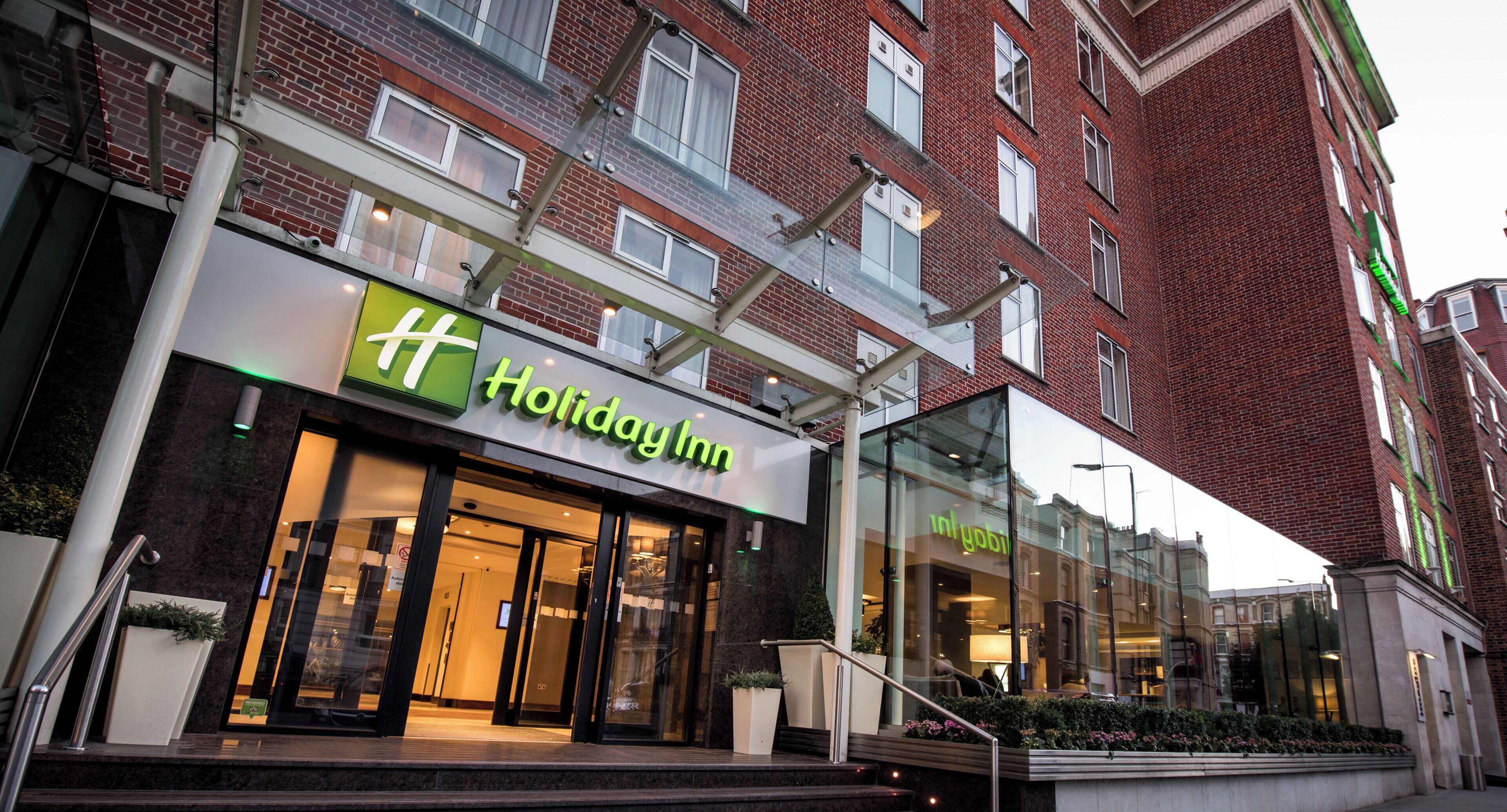 A Holiday Inn hotel with a modern facade, large glass windows, and a brick building in the background.