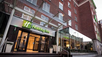 A Holiday Inn hotel with a modern facade, large glass windows, and a brick building in the background.