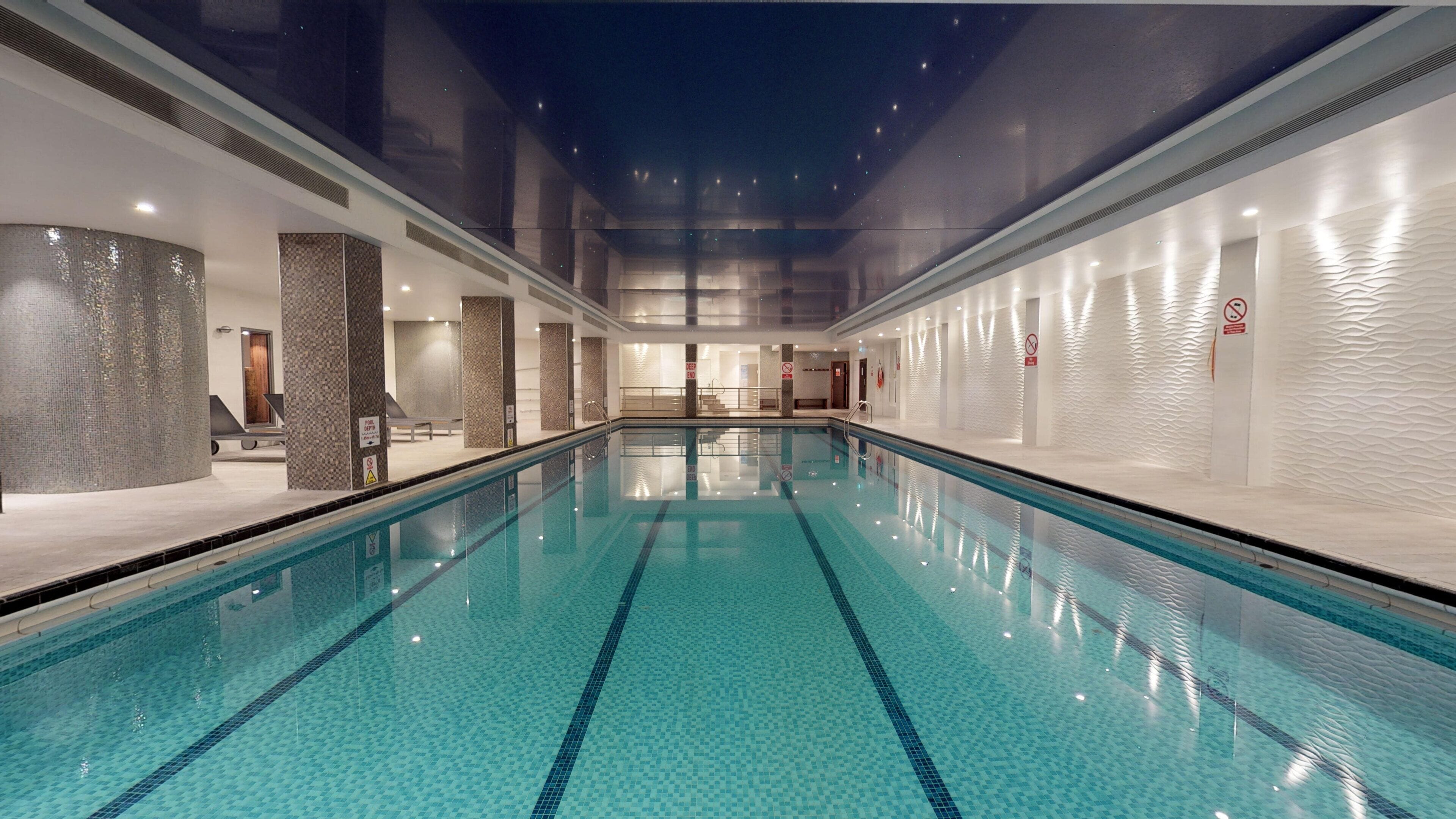 A large indoor swimming pool with clear water, surrounded by walls with textured patterns, and a ceiling with a starry design.
