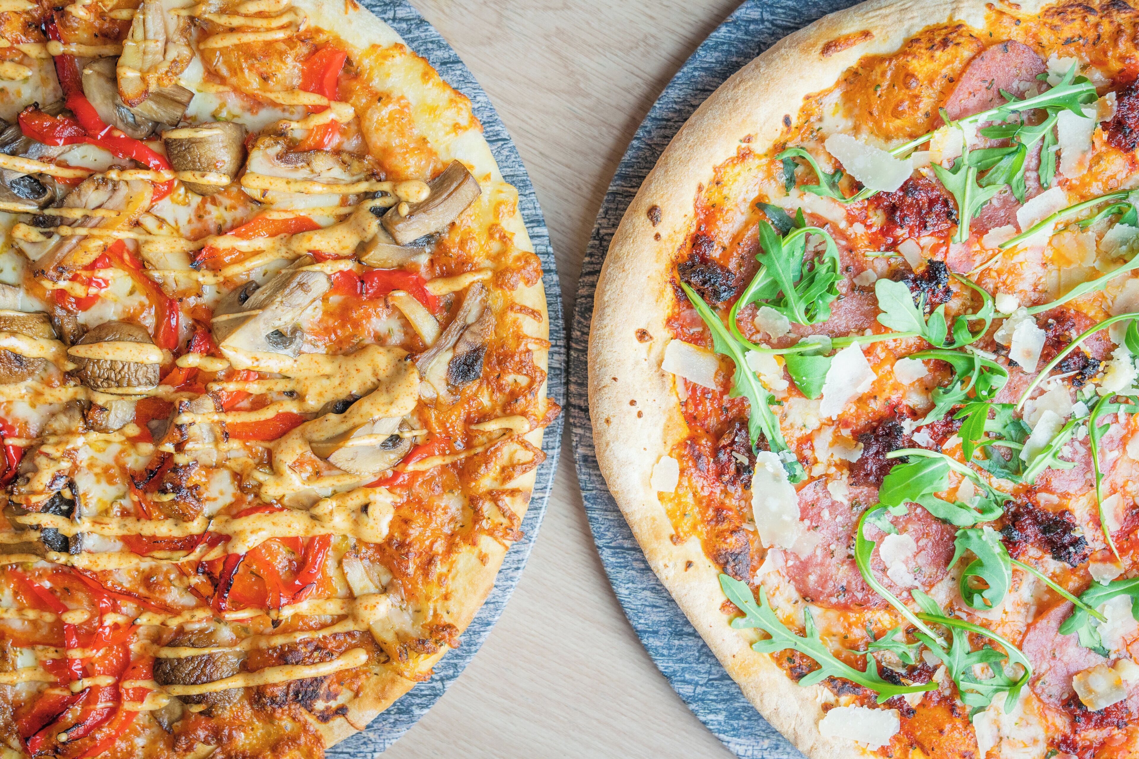 Twee pizza's met diverse toppings op een houten tafel.