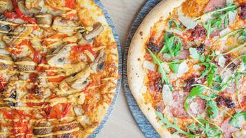 Twee pizza's met diverse toppings op een houten tafel.
