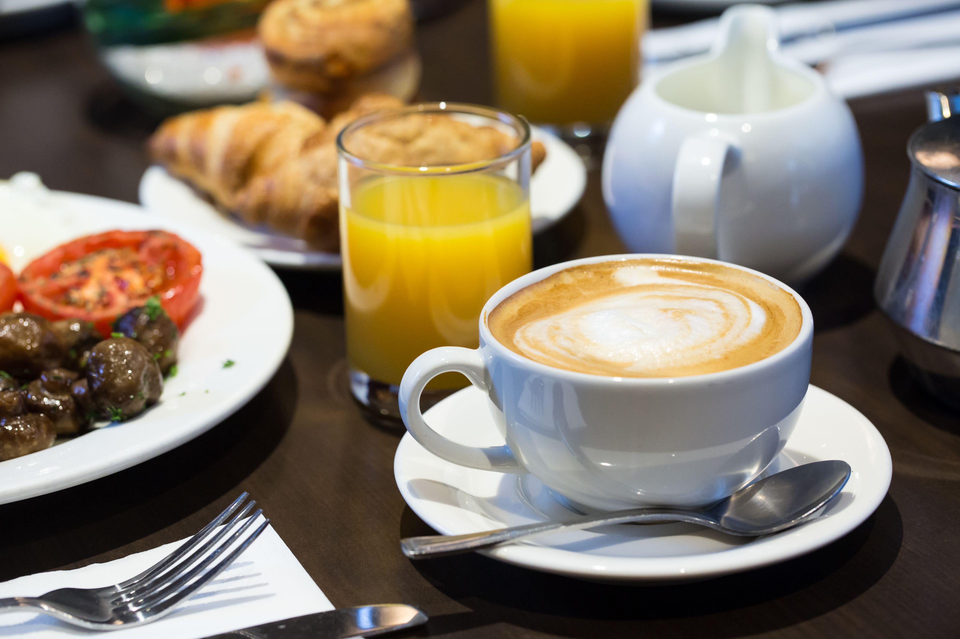 A breakfast setting with croissants, a glass of orange juice, a coffee cup, and a teapot on a table.