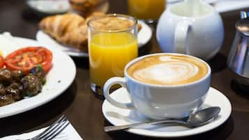 A breakfast setting with croissants, a glass of orange juice, a coffee cup, and a teapot on a table.