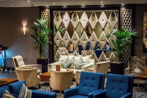 A hotel lobby with a seating area, a decorative wall, and potted plants. - Holiday Inn London - Kensington High St. by IHG (London)