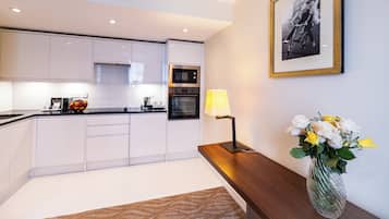 A modern kitchen with white cabinets, a microwave, and a stove. There is a vase with flowers on a wooden table.