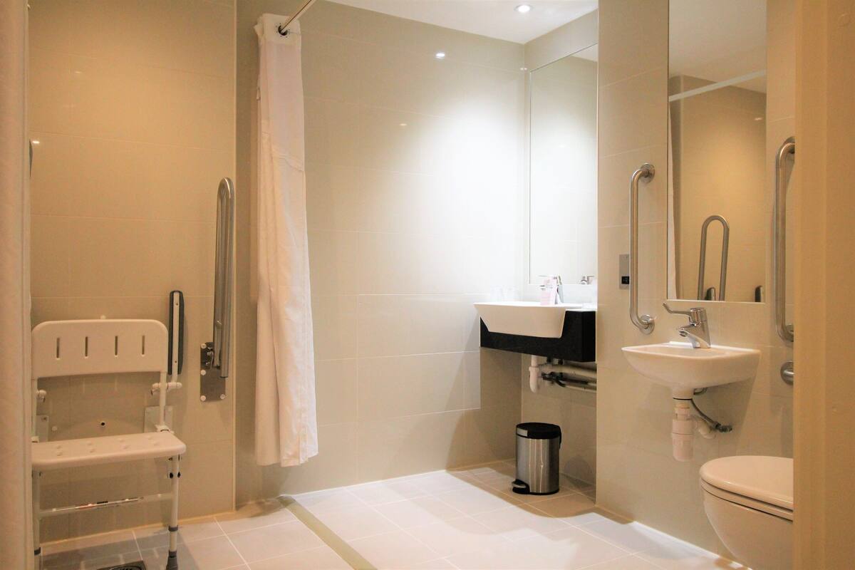 Un bagno moderno dotato di doccia, toilette, lavandino e maniglia di sostegno.