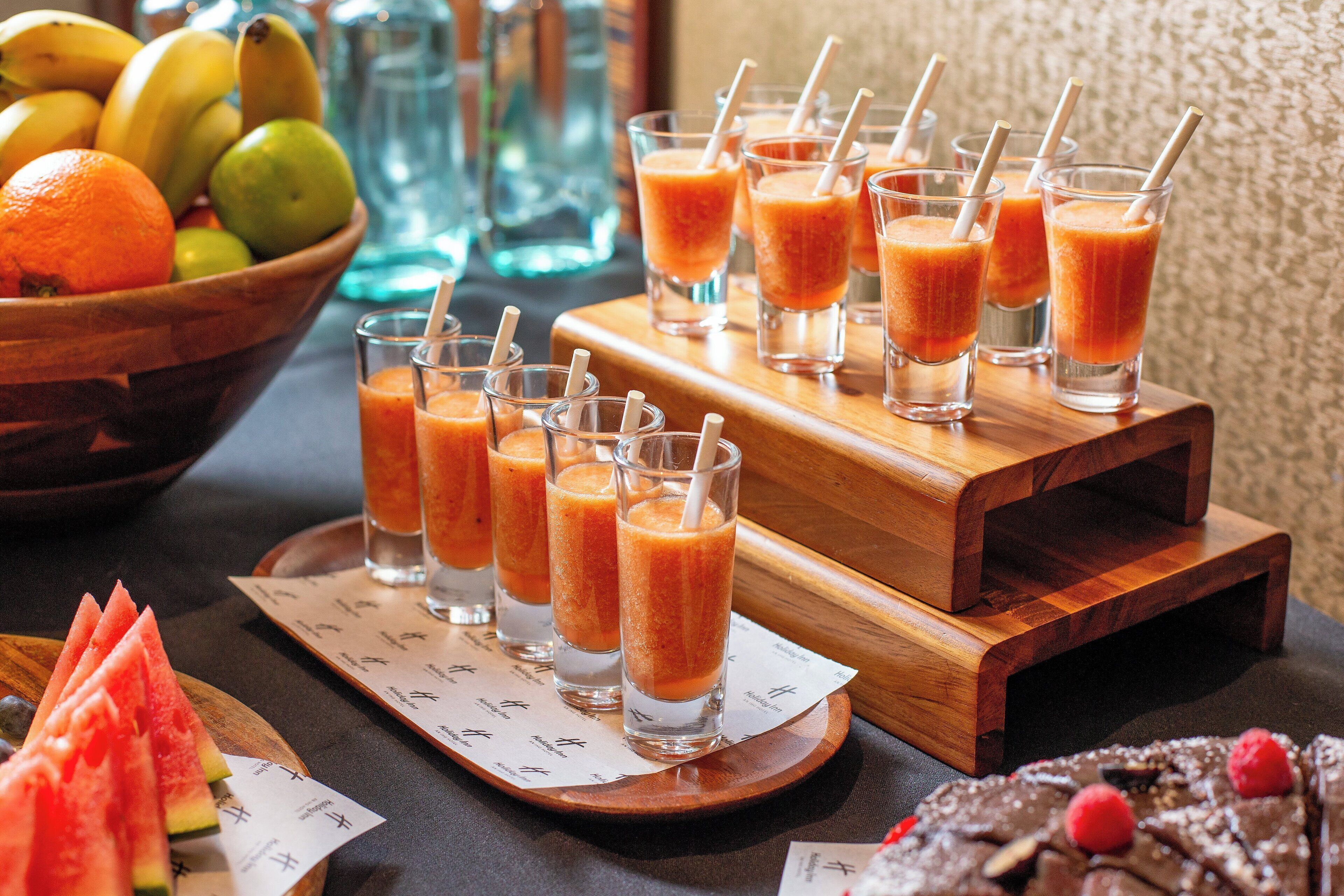 Ein Tisch mit mehreren Gläsern Orangensaft, einer Obstschale und einer Platte mit Wassermelone.