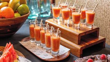 Une table avec plusieurs verres de jus d’orange, un saladier de fruits et un plateau de tranches de pastèque.