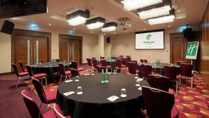 A conference room with round tables, red chairs, and a large screen displaying the Holiday Inn logo.