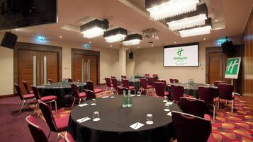 A conference room with round tables, red chairs, and a large screen displaying the Holiday Inn logo.