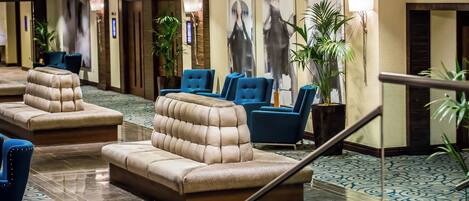 A hotel lobby with seating areas, a staircase, and a patterned floor.
