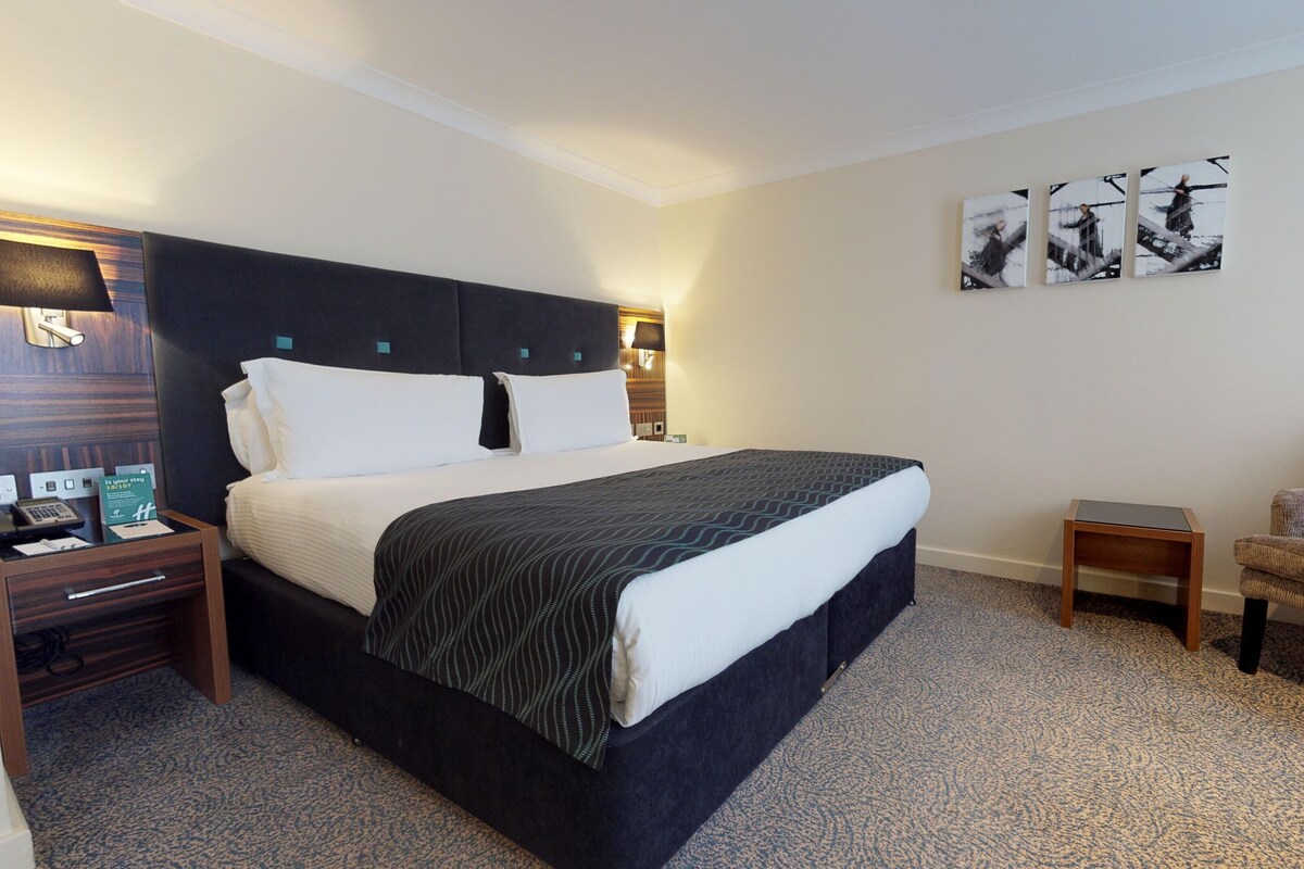 Une chambre d’hôtel avec un grand lit, des tables de chevet, une chaise et des œuvres d’art accrochées au mur.