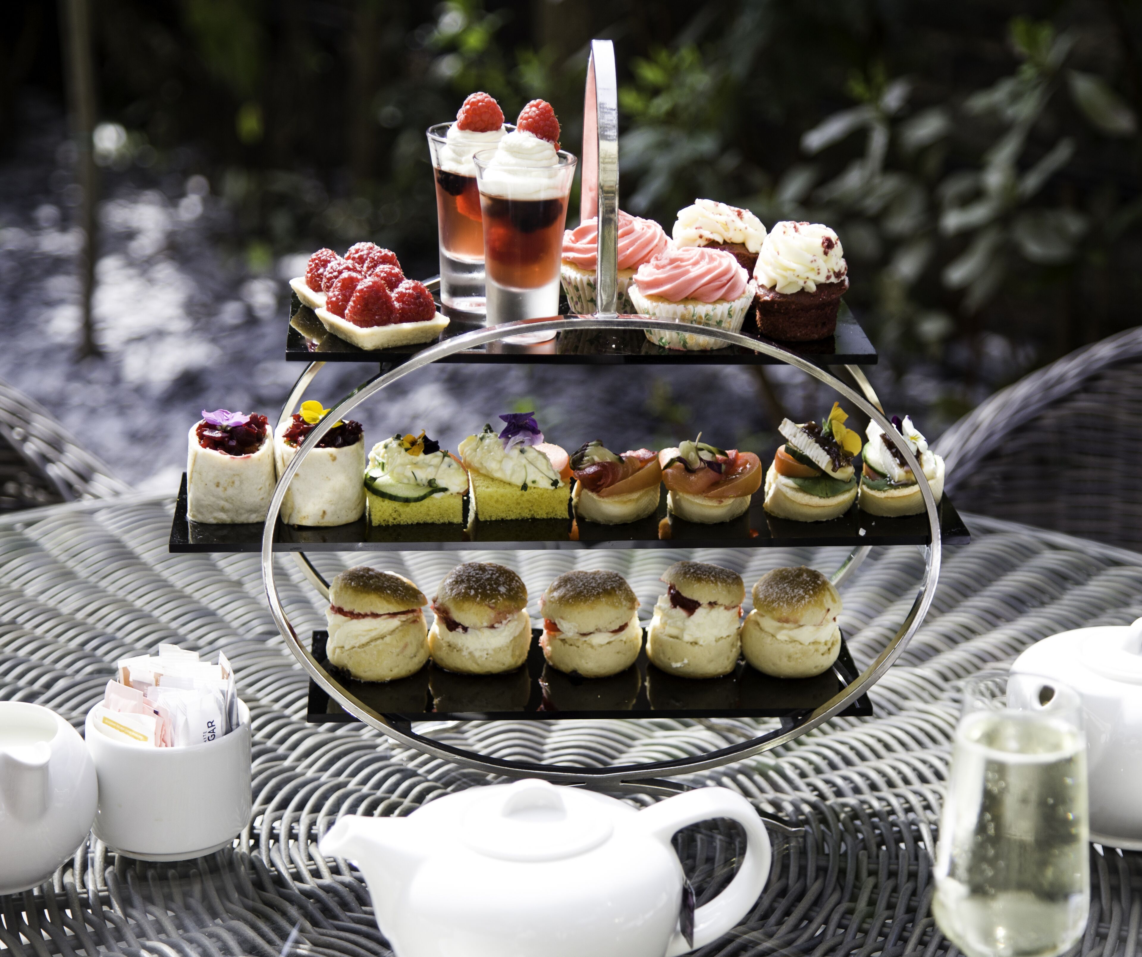 A tiered dessert stand with various pastries and a tea glass on a wicker table.