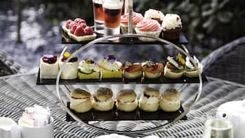 Un présentoir à étages garni de diverses pâtisseries et une tasse à thé posée sur une table en osier.