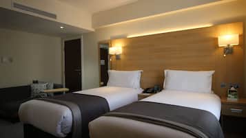 A hotel room with two beds, a bedside table, a lamp, a phone, and a small table with a chair.