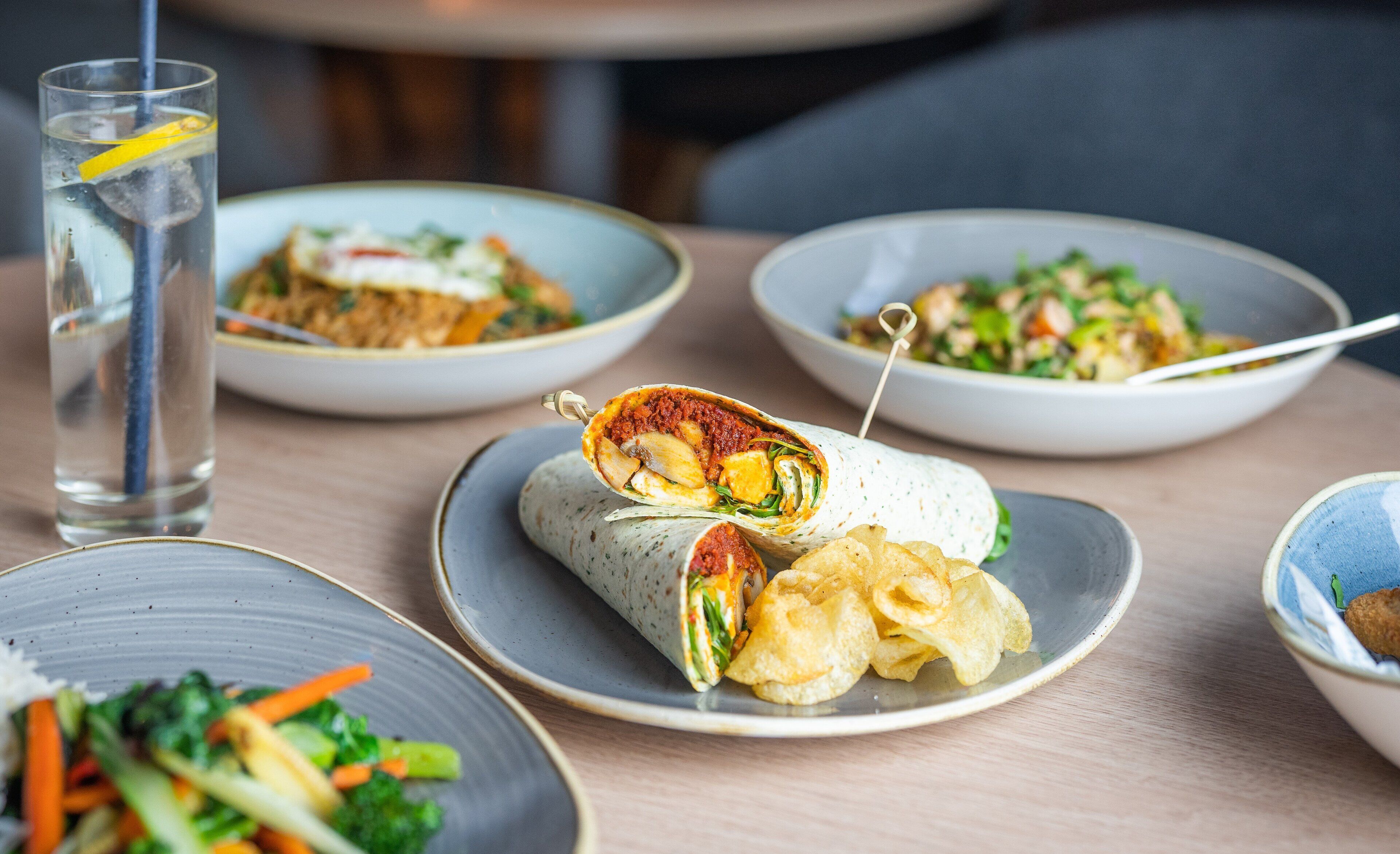 Une table où l’on trouve différents plats, notamment un wrap, une salade et un bol de frites.