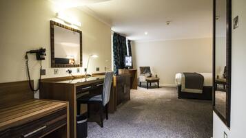 Une chambre d’hôtel avec un bureau en bois, une chaise, un lit, une télévision et un miroir.