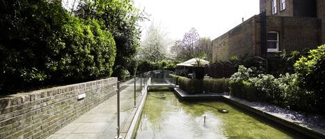 A narrow water feature with a brick wall on one side and a building on the other.