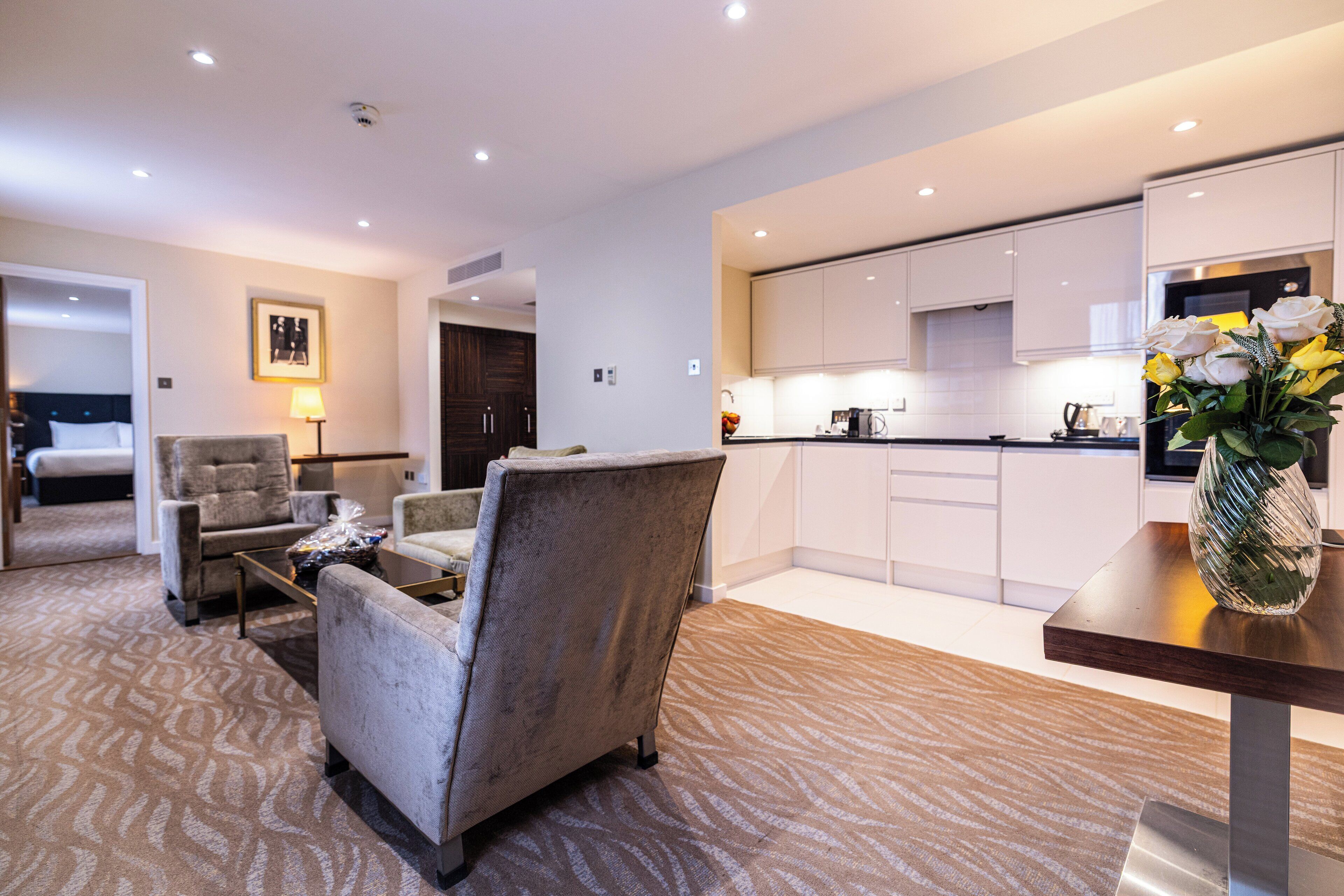 A modern hotel room with a living area, a dining table, and a kitchen.
