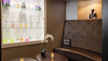 Un moderno espacio de spa con una vitrina de productos para el cuidado de la piel, una zona de estar con un banco acolchado y una estatua sobre una estantería.