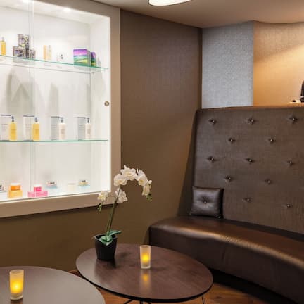 A modern spa area with a glass display of skincare products, a seating area with a cushioned bench, and a statue on a shelf.