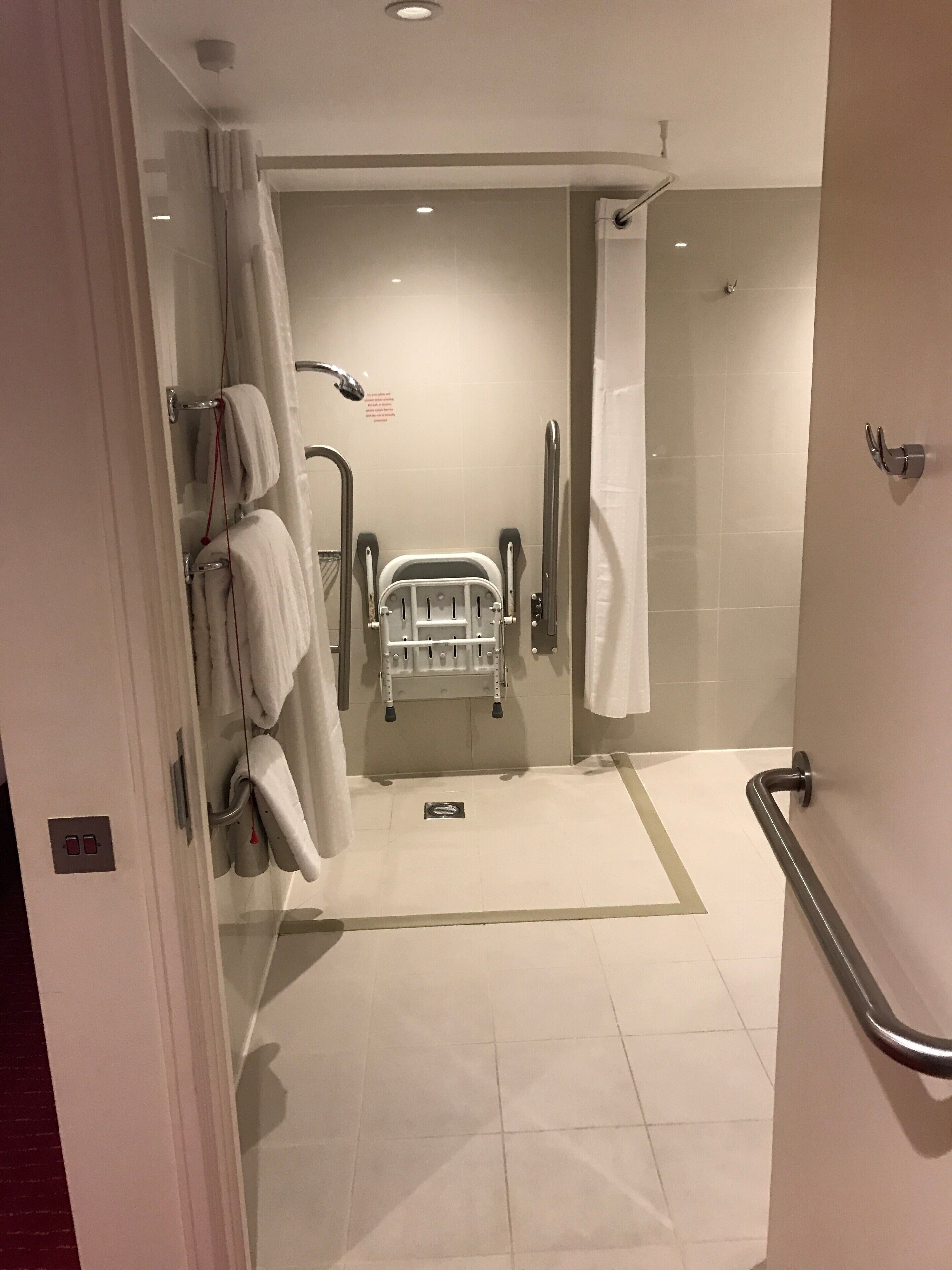 A modern bathroom with a shower, grab bars, and a wheelchair-accessible shower chair.